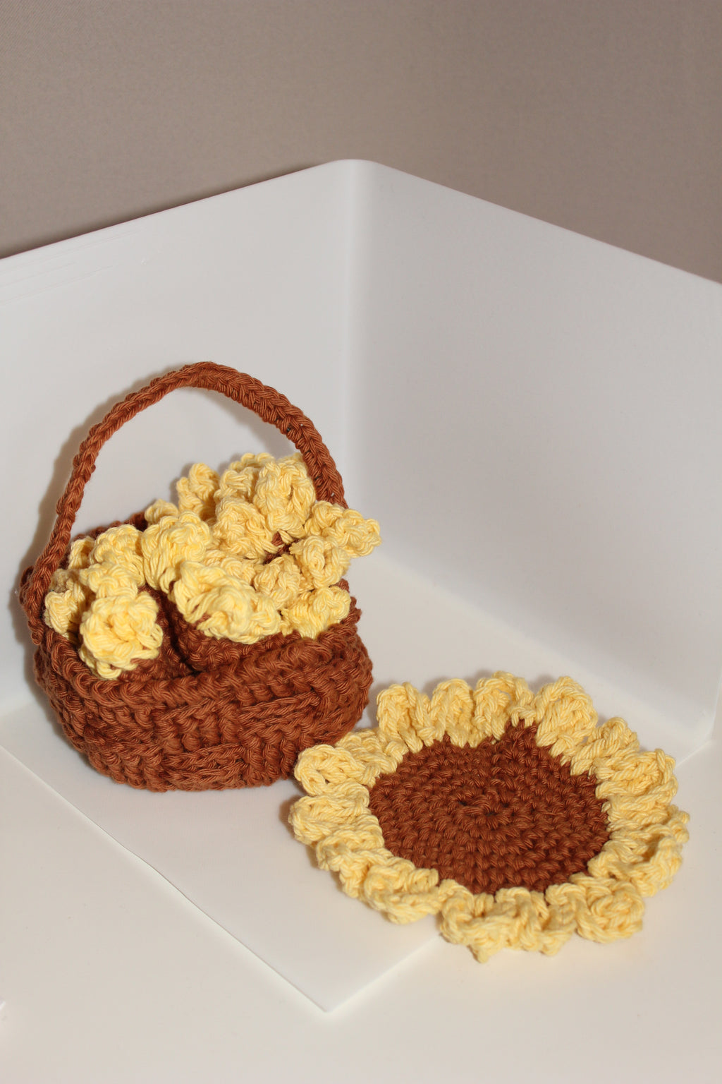 Crocheted brown basket with 3 yellow sunflower coaster inside and 1 laying on a white background
