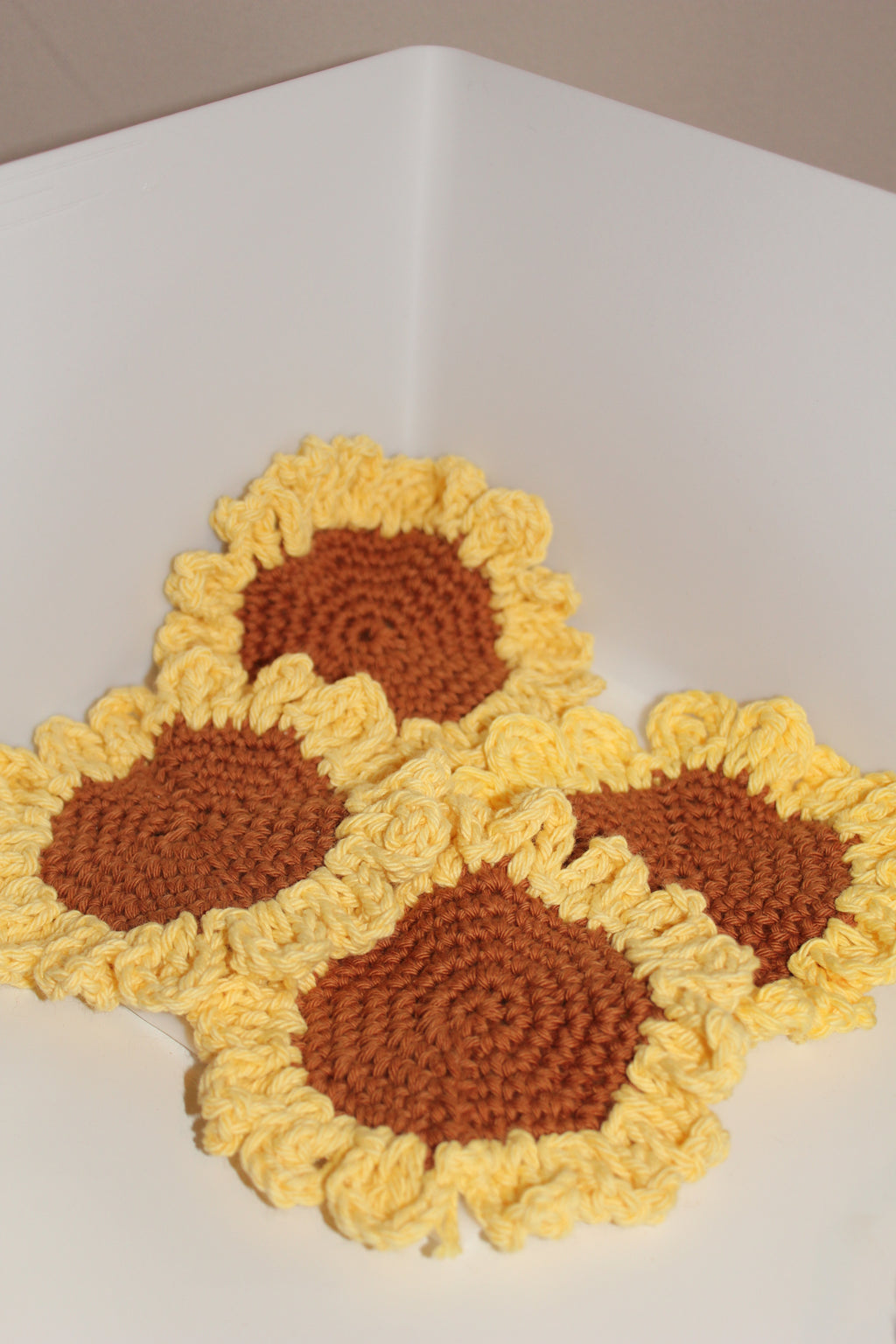 Crocheted sunflower coasters with yellow petals and brown centers on a white surface.
