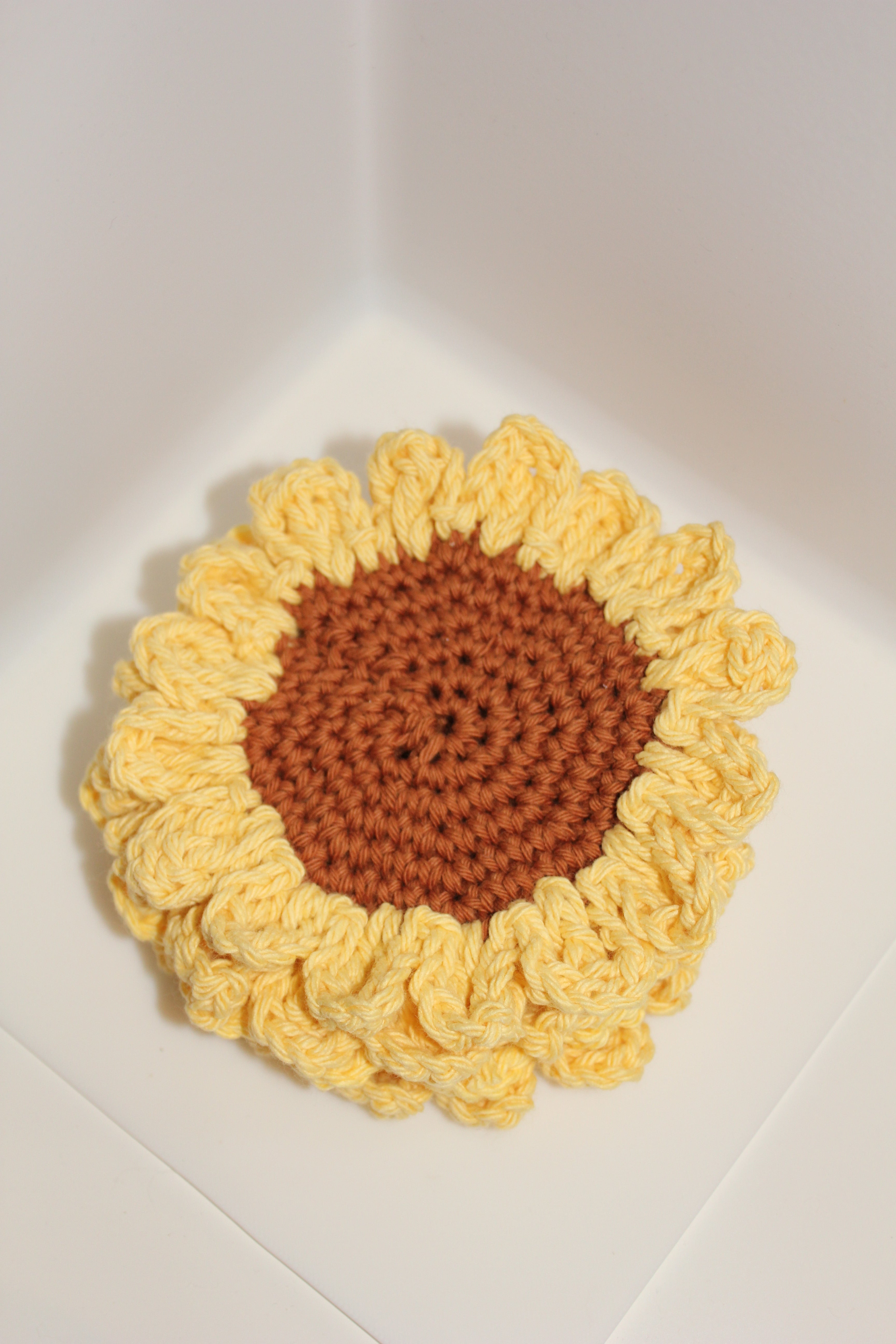 4 stacked crocheted sunflower coaster with yellow petals and brown center on a white surface