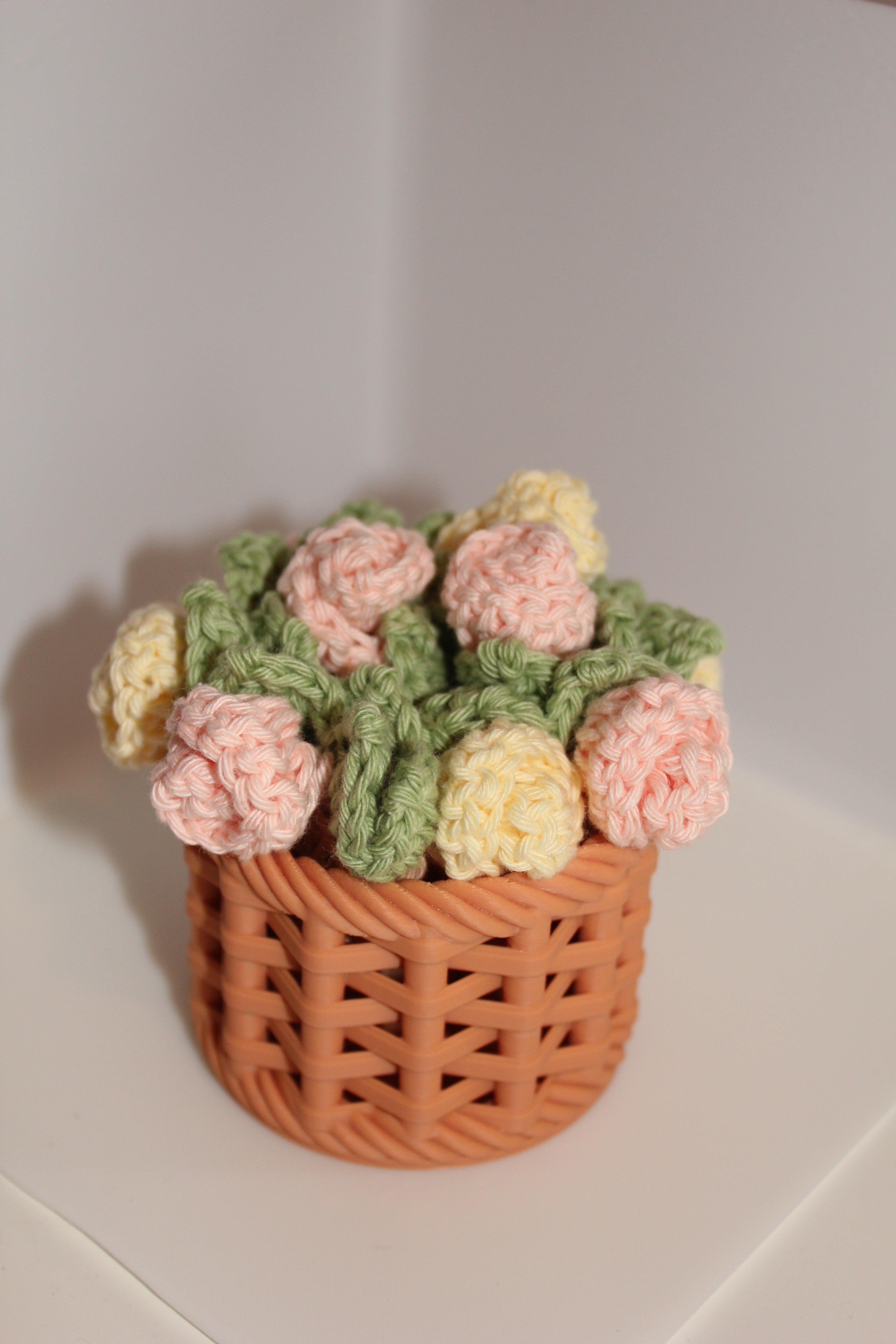 Knitted flower basket with pink & yellow roses and green leaves on a white background
