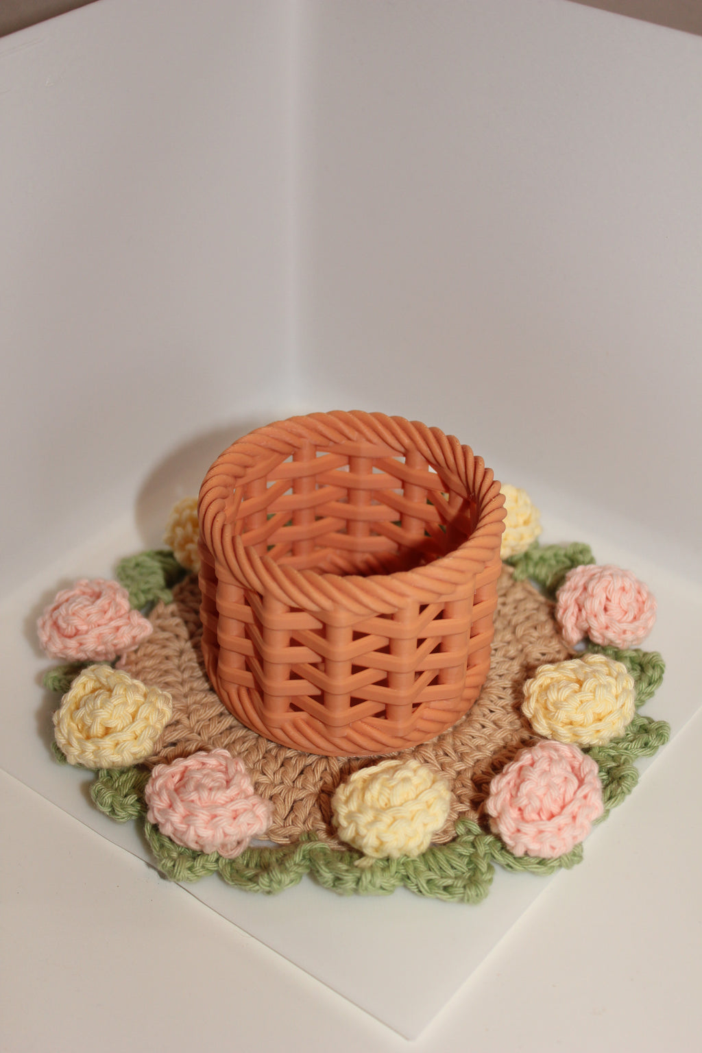 Knitted flower basket on top of coaster with pink & yellow roses and green leaves on a white background