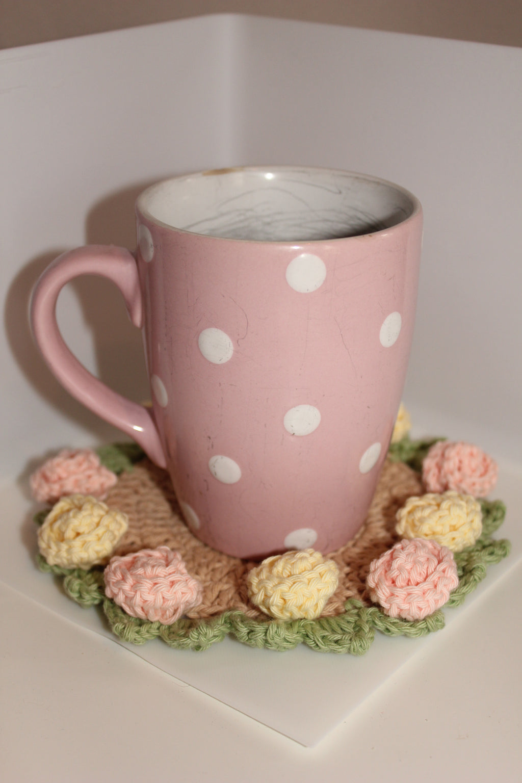 Pink polka dot mug on pink & yellow roses coaster and green leaves on a white background