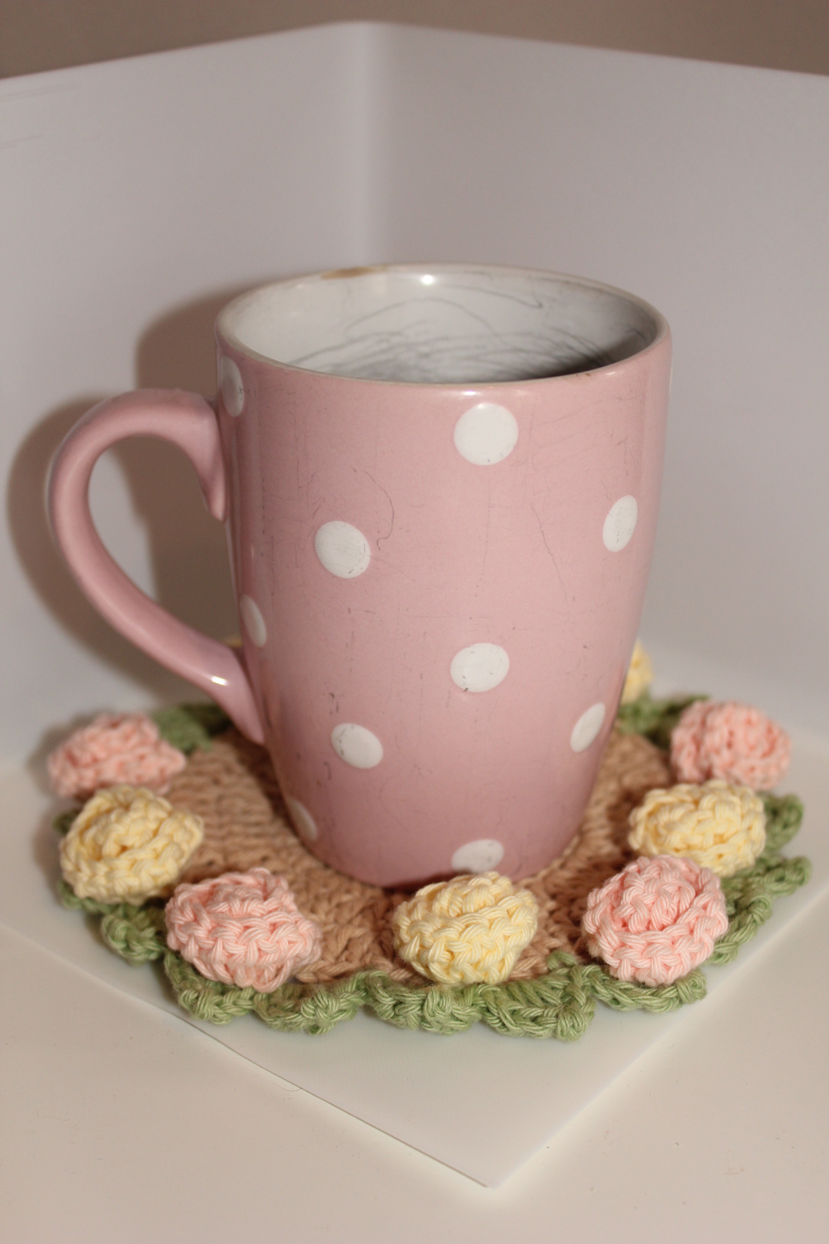 Pink polka dot mug on pink & yellow roses coaster and green leaves on a white background