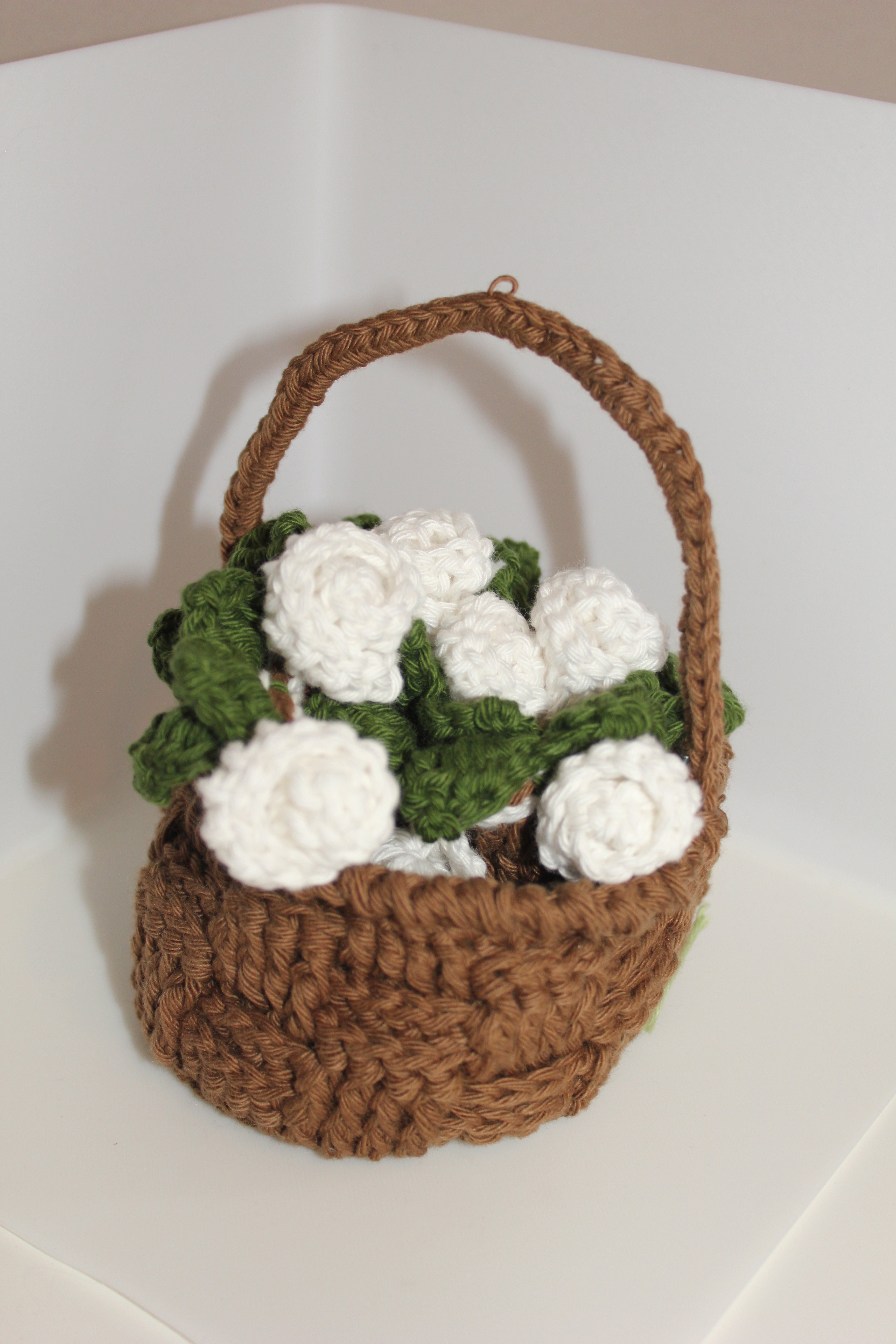 Crocheted brown basket with rolled up coaster with white roses green leaves in basket