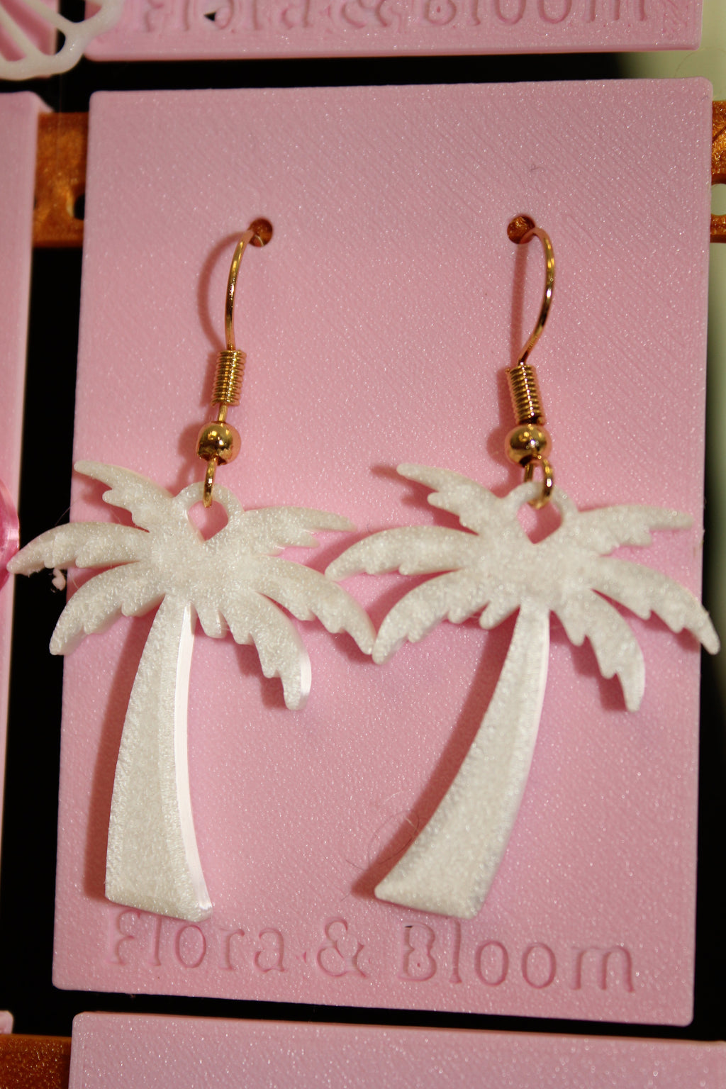 White palm tree earring with gold hooks on a pink "Flora & Bloom" card