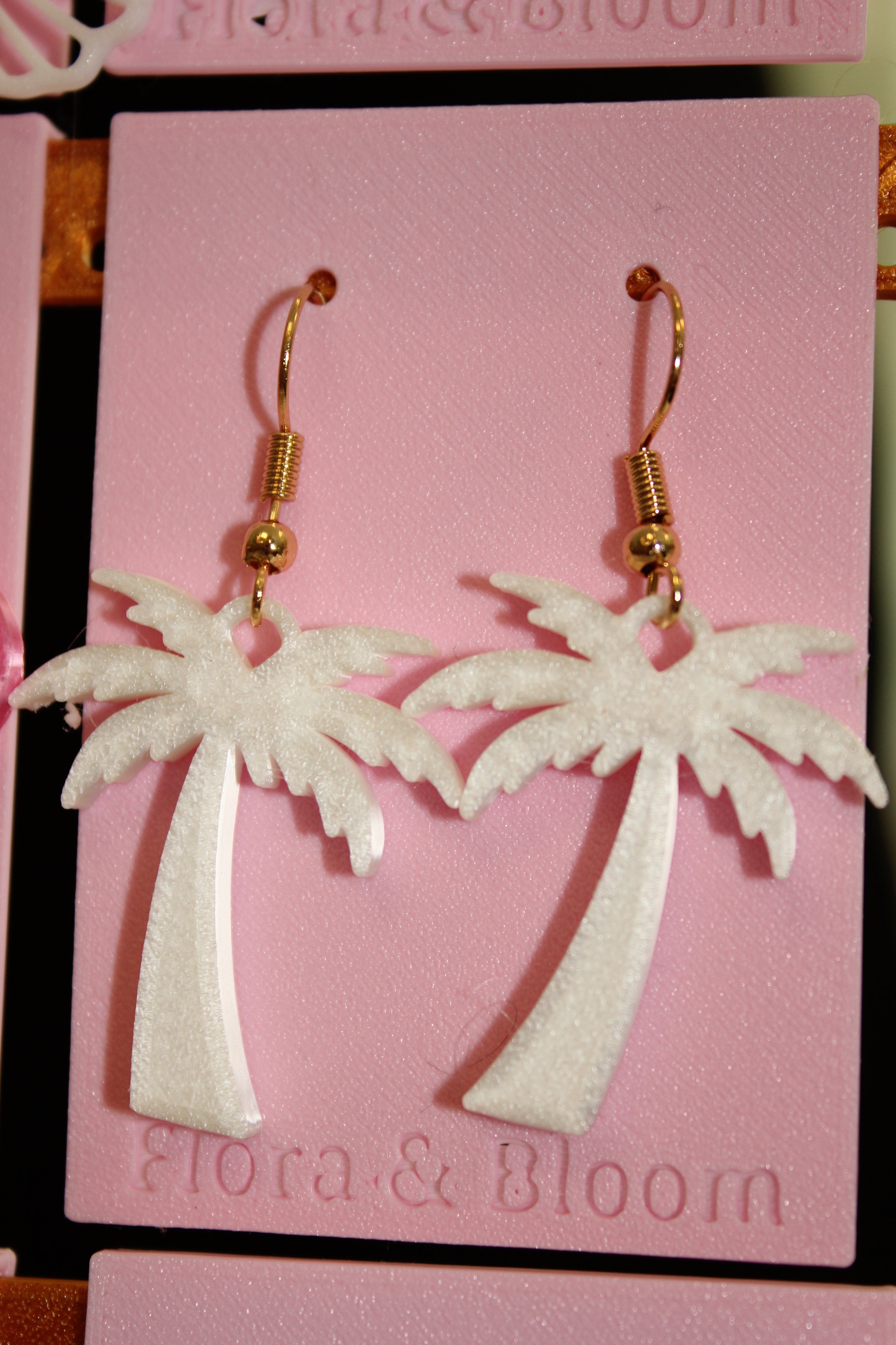White palm tree earring with gold hooks on a pink "Flora & Bloom" card